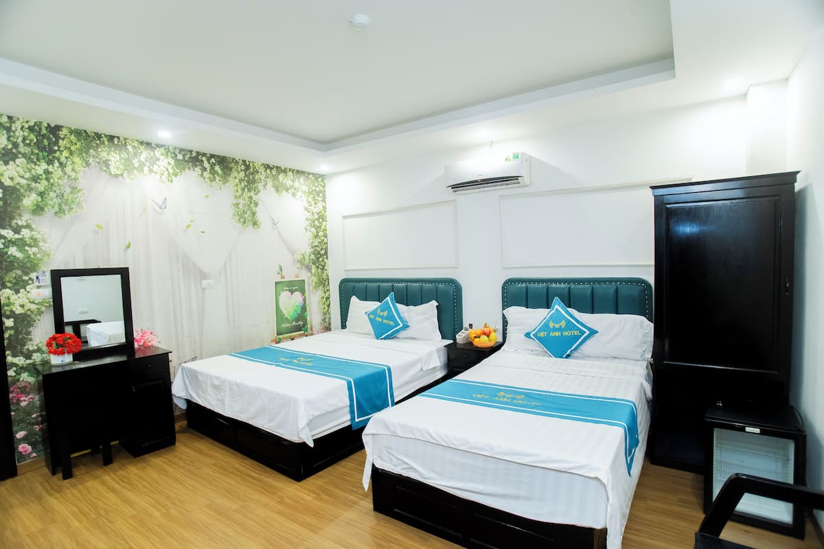 A hotel room with two beds, a TV, a desk, and a mirror.