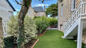 A stone building with a staircase, a small lawn, and a tree.