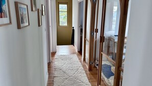 A hallway with framed pictures, a wooden floor, a white rug, and a sliding glass door leading to a room.
