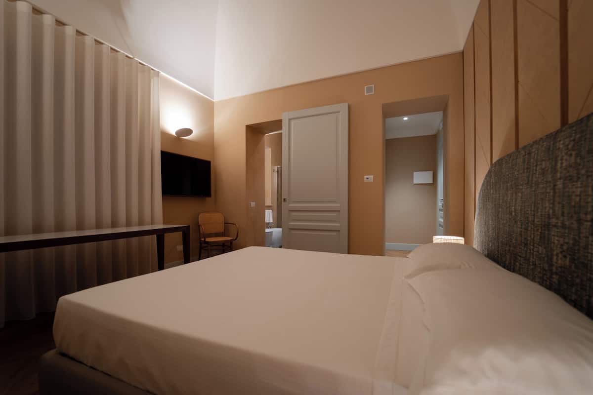 A hotel room with a bed, a chair, a TV, and a door leading to another room.