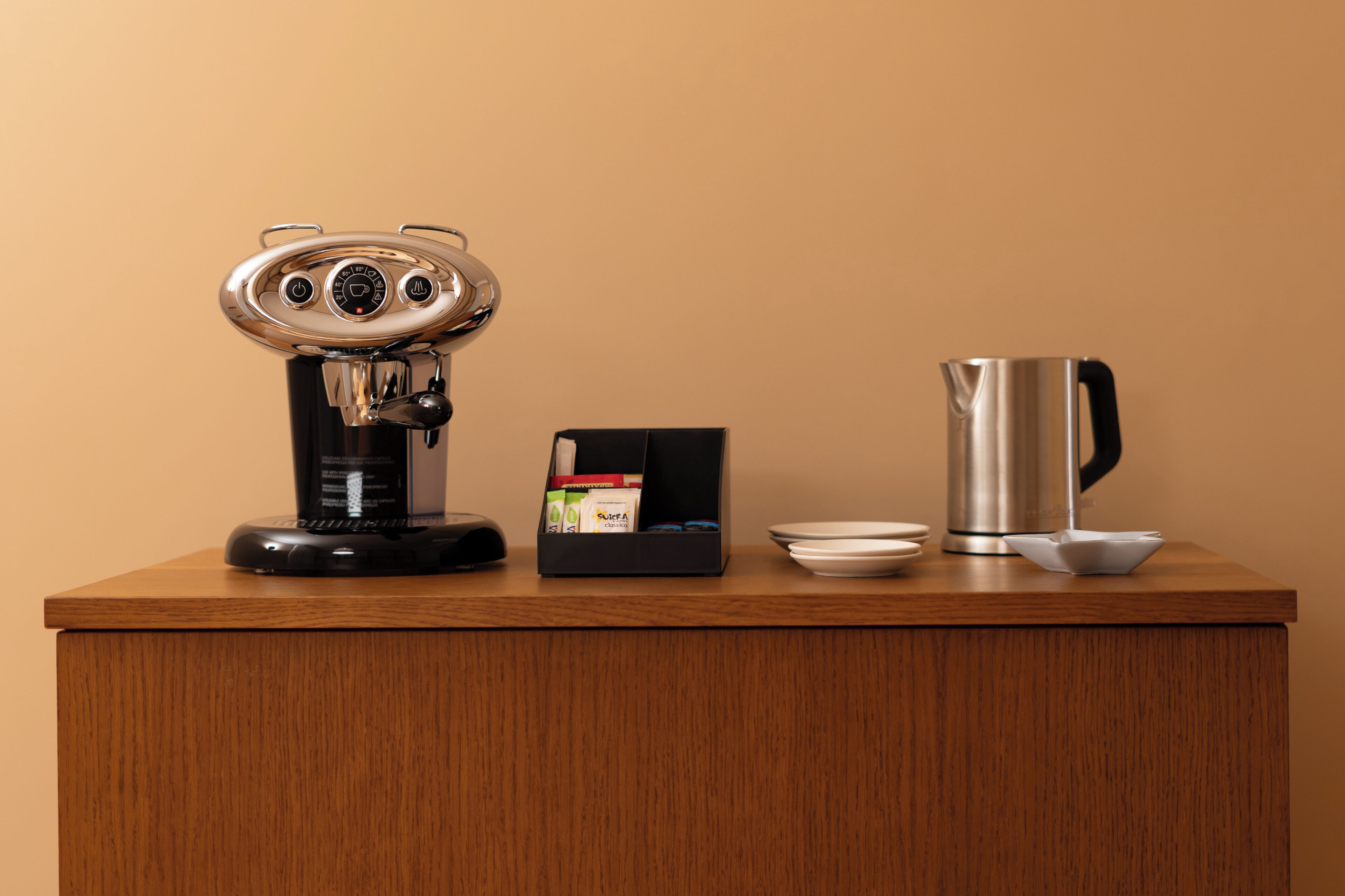 A coffee machine, a box of coffee pods, a coffee pot, and a cup on a wooden counter.