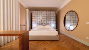 Une chambre à coucher avec un lit, un plancher en bois, des rideaux, un miroir et un papier peint à motifs.