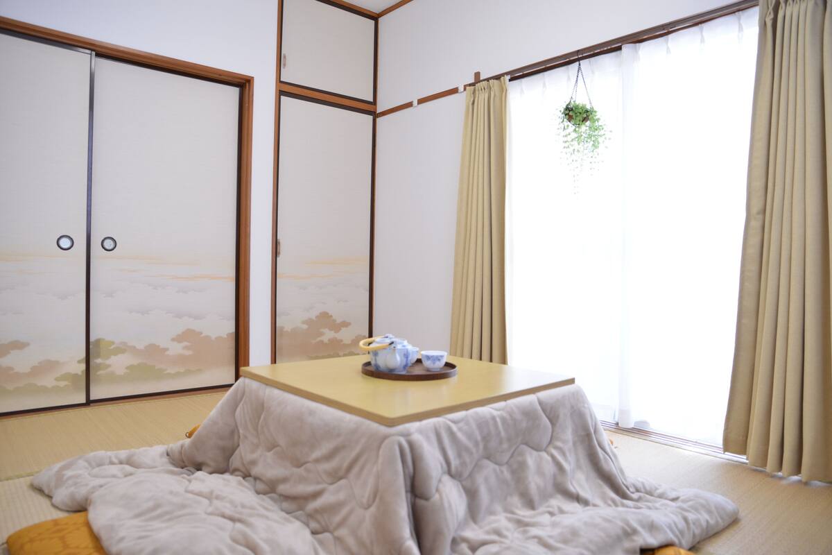 A traditional Japanese room with tatami flooring, a low table with a tea set, sliding doors, and a hanging plant.