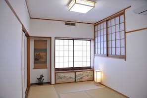 A traditional Japanese room with tatami flooring, a shoji screen door, and a hanging artwork. - Green House (Tokyo)