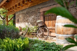 A rustic building with a stone wall, a wooden door, a large barrel, and a bicycle with a basket. - Holiday Home Hofgut Wörner – Ground Floor Apartment / Kneipp / Vineyards / Terrace / Winery (Durbach)
