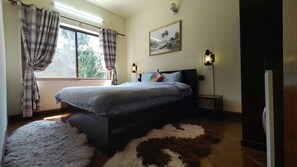 A bedroom with a bed, a window with curtains, a nightstand, a wall-mounted lamp, and a painting. - Perfect 3-bedroom apartment in gorgeous Kathmandu with fitness room (Kathmandu)