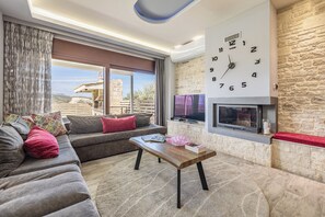 A modern living room with a sofa, a wooden coffee table, a fireplace, and a large wall clock. - Stone Build Modern and Traditional Villa near Heraklion (Agios Syllas)