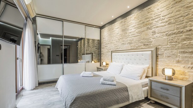 A modern bedroom with a large bed, a nightstand, a mirror, and a stone wall. - Stone Build Modern and Traditional Villa near Heraklion (Agios Syllas)