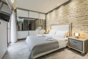 Quarto moderno com uma cama grande, mesa de cabeceira, espelho e parede de pedra.