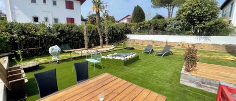 A backyard with a wooden table, two lounge chairs, a barbecue grill, and a small pool.