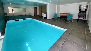 Ein Schwimmbad mit gefliestem Boden, ein Essbereich mit Stühlen, einer Couch und einem Fernseher.