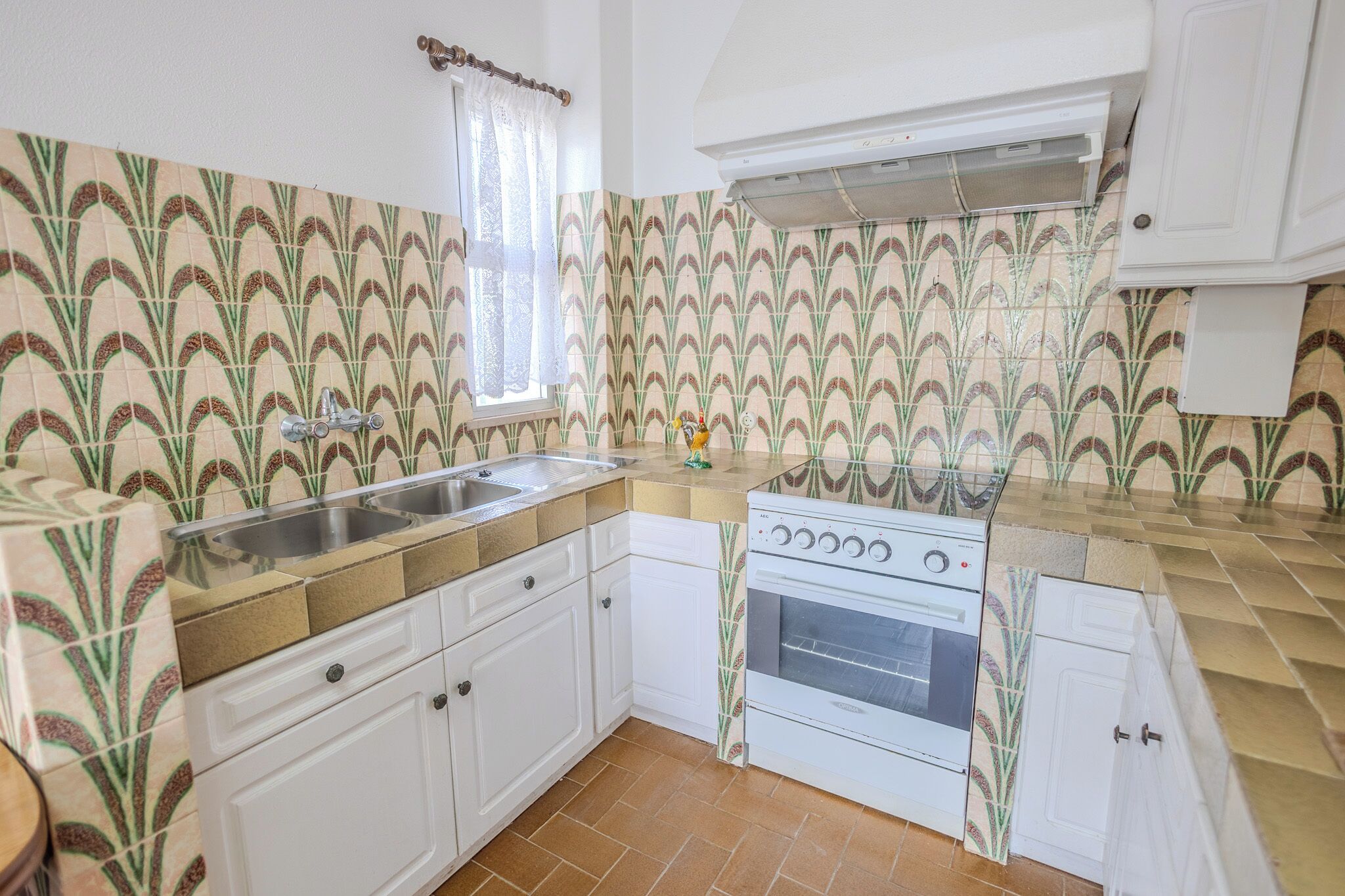 A kitchen with white cabinets, a sink, a stove, and patterned tiles.