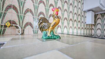 Un gallo in ceramica su un pavimento piastrellato, con una parete decorata sullo sfondo.