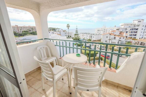 A balcony with white chairs and a small table, overlooking a residential area with buildings and a clear sky. - Casa das Pedras by Umbral  (Albufeira)
