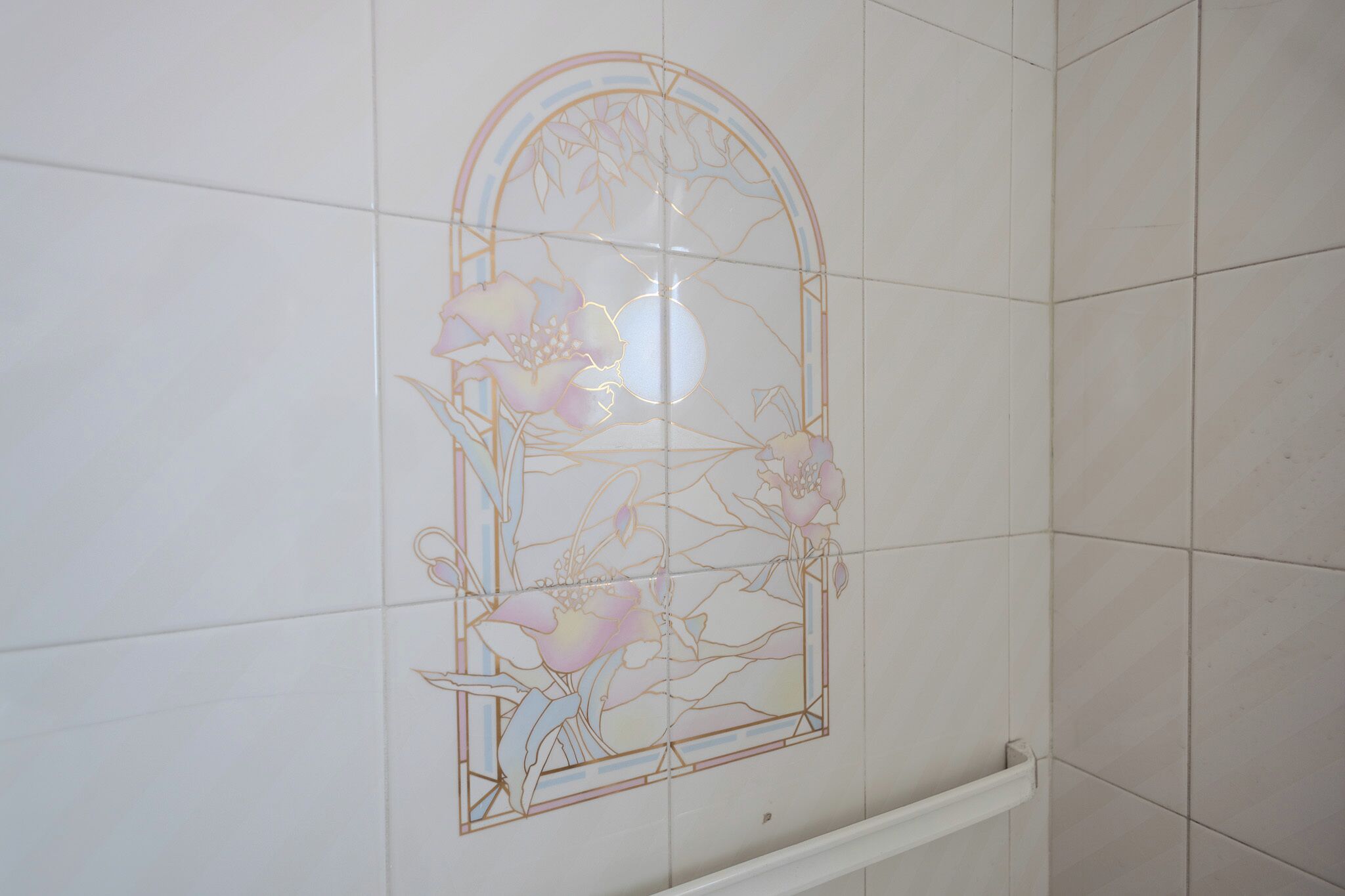 A bathroom with white tiled walls and a decorative stained glass window.