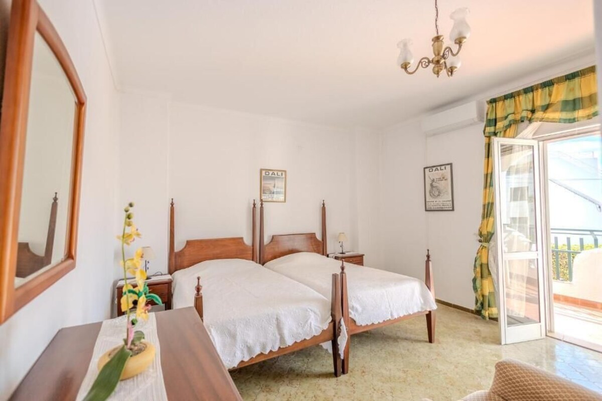 A bedroom with two single beds, a wooden headboard, a nightstand with a lamp, a mirror, and a window with curtains.