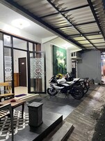 Una motocicleta estacionada en un espacio cubierto con piso de baldosas, un banco y un bote de basura.