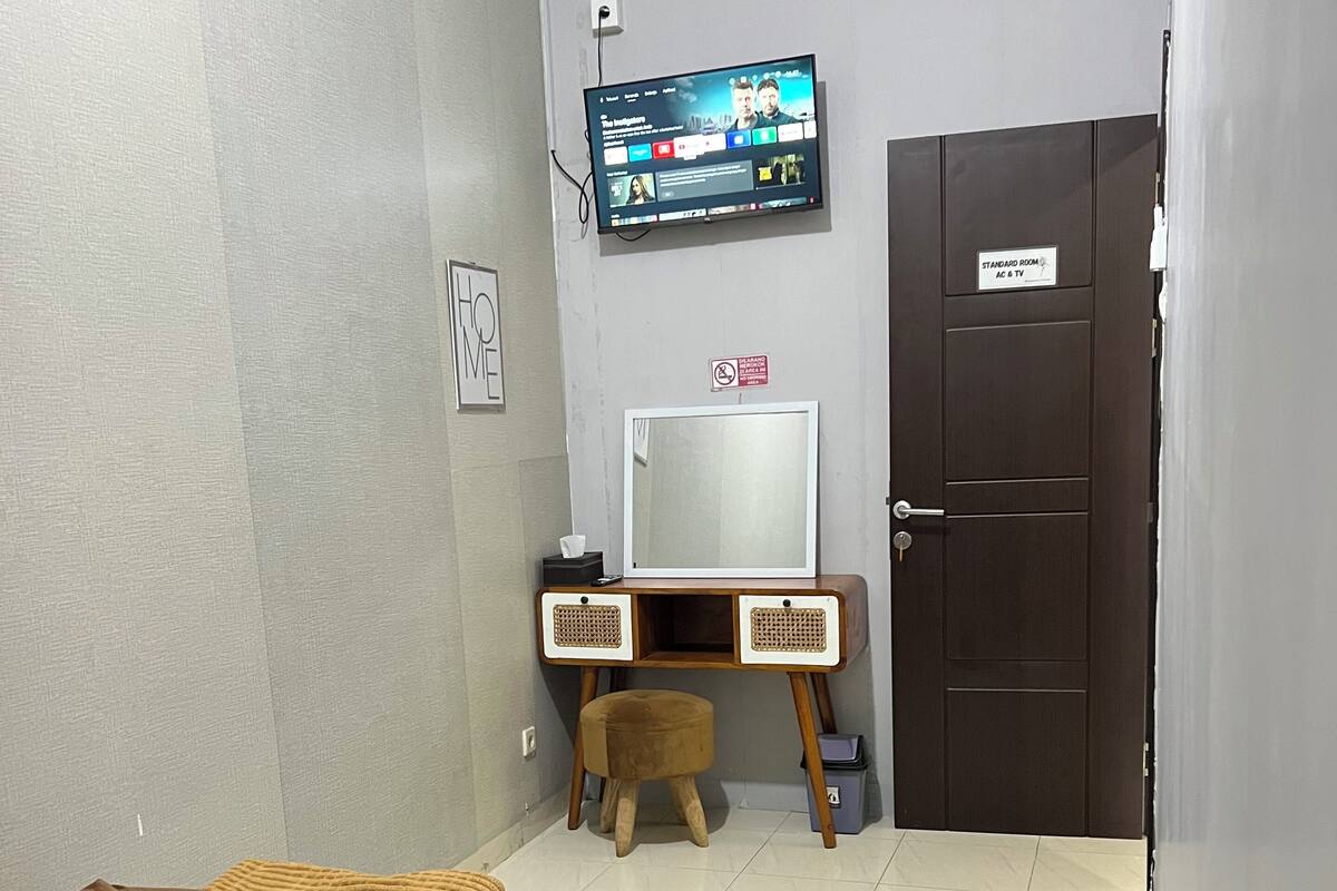Une pièce comprenant un lit, un bureau avec une télévision, une porte et un petit tabouret.