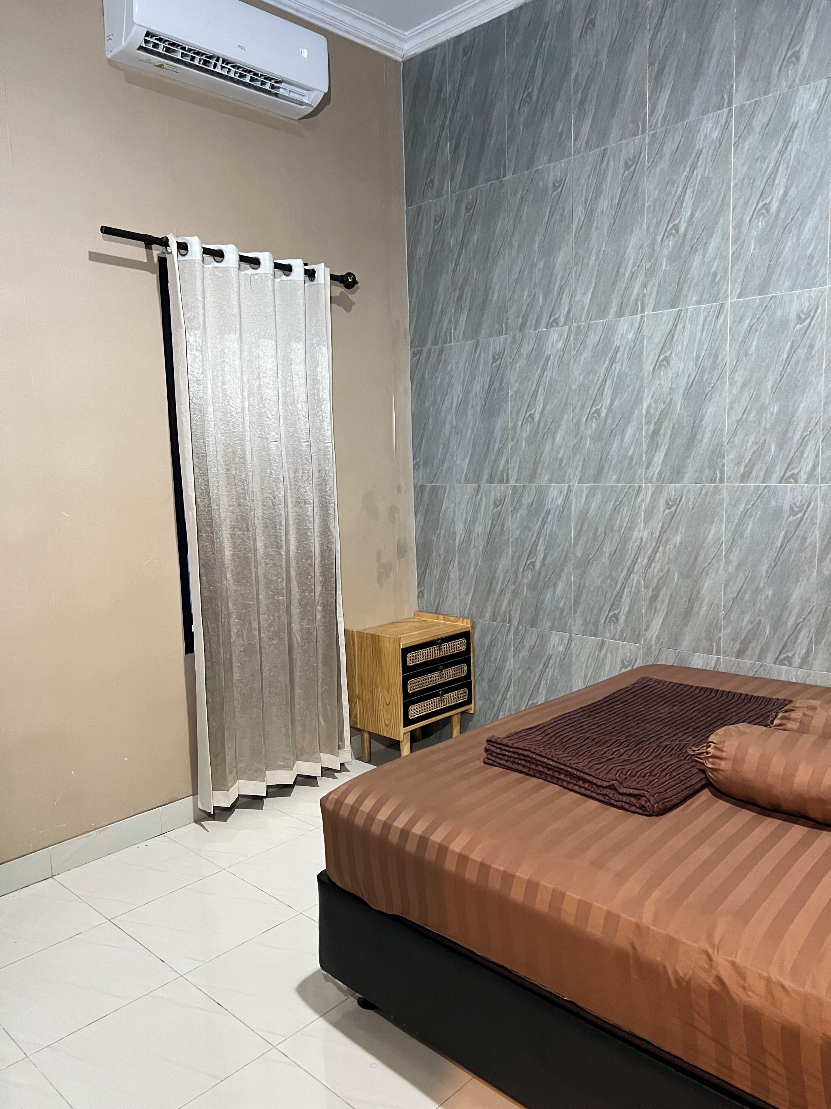 Une chambre à coucher comprenant un lit, un rideau, un climatiseur fixé au mur et une petite armoire en bois.