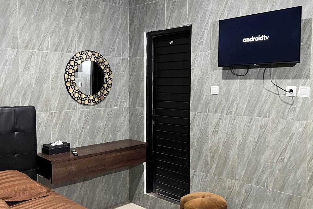 Une chambre à coucher moderne avec un lit, un téléviseur fixé au mur, un miroir et un banc en bois.