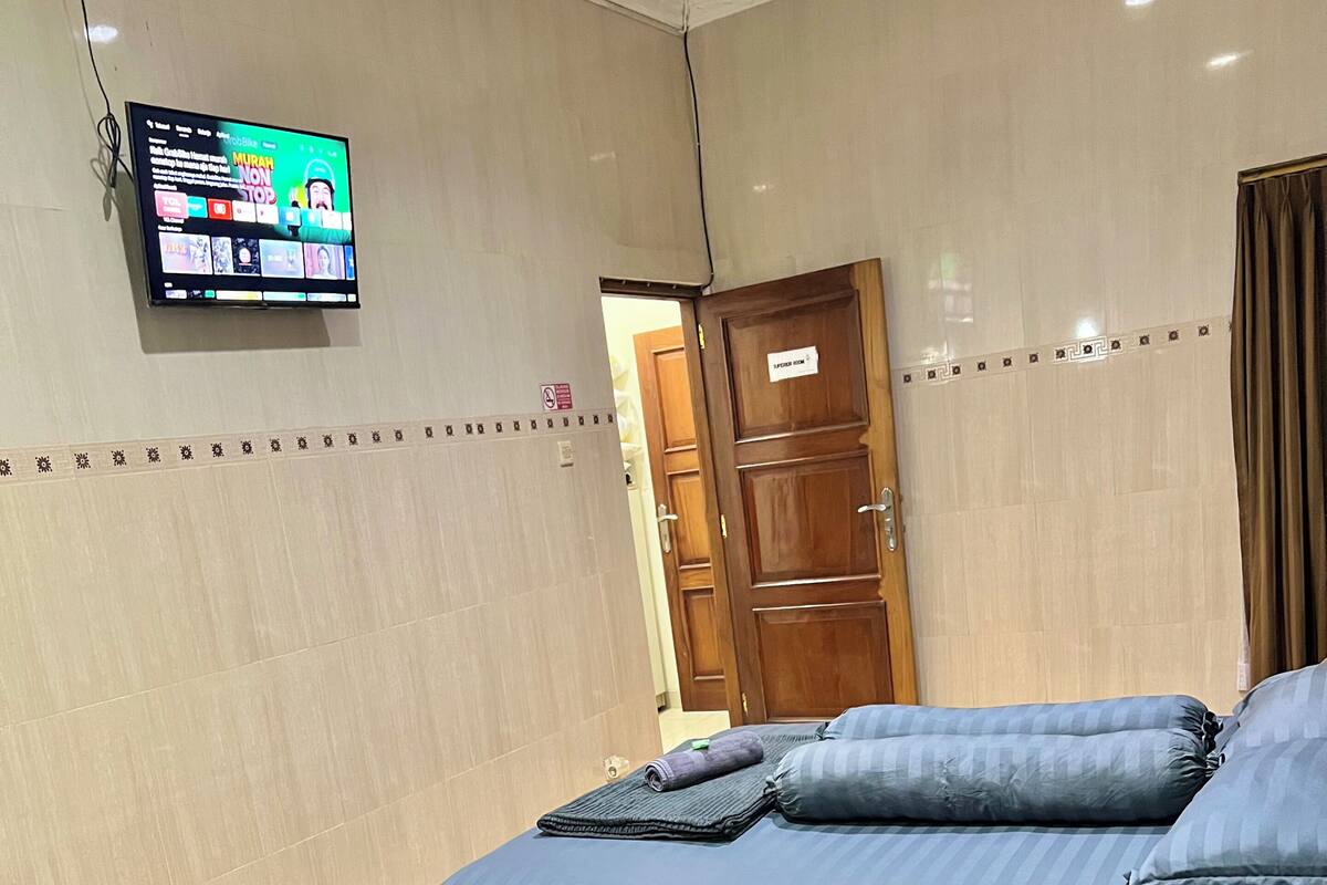 Une chambre d’hôtel avec deux lits, un téléviseur fixé au mur et une porte en bois.