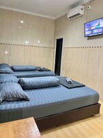 Una habitación de hotel con una cama grande, un televisor de pantalla plana en la pared y un equipo de aire acondicionado.