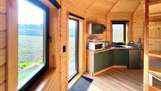 A wooden cabin interior with a kitchen area, large windows, and a view of the outdoors.