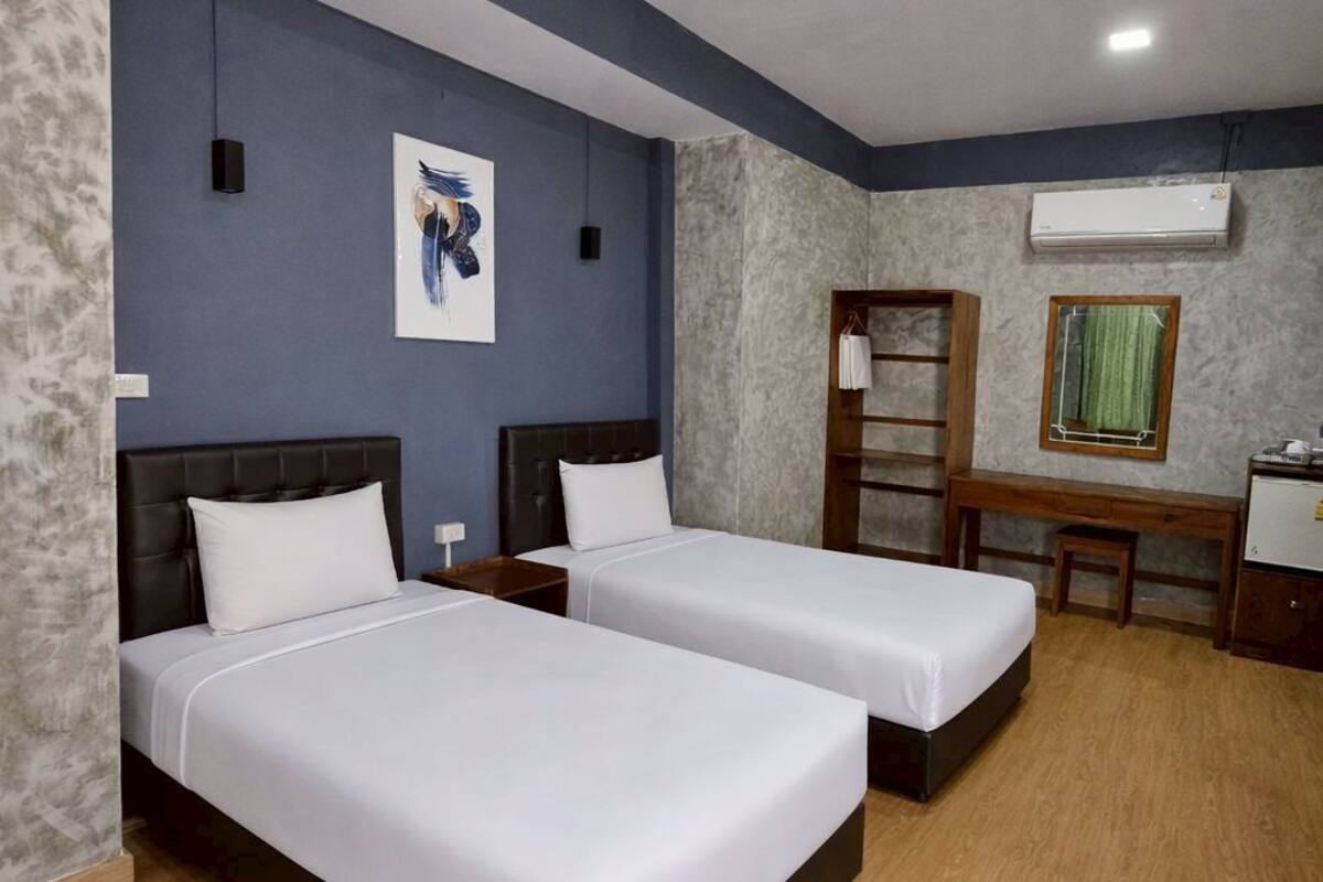 A hotel room with two beds, a desk, a chair, an air conditioning unit, and a wall-mounted mirror.