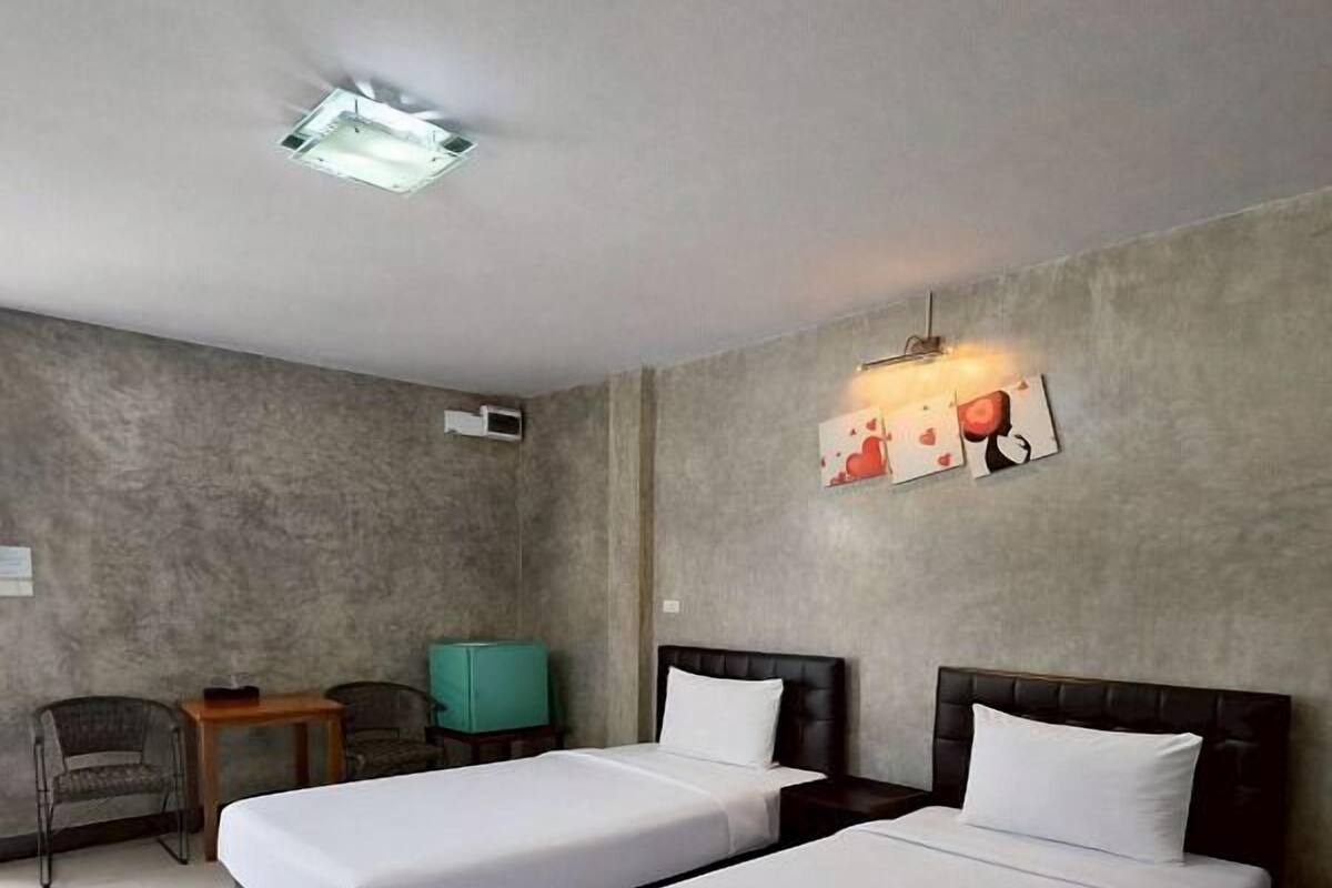 A hotel room with two beds, a small table, a chair, and a wall-mounted light fixture.