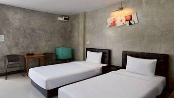 A hotel room with two beds, a small table, a chair, and a wall-mounted light fixture.