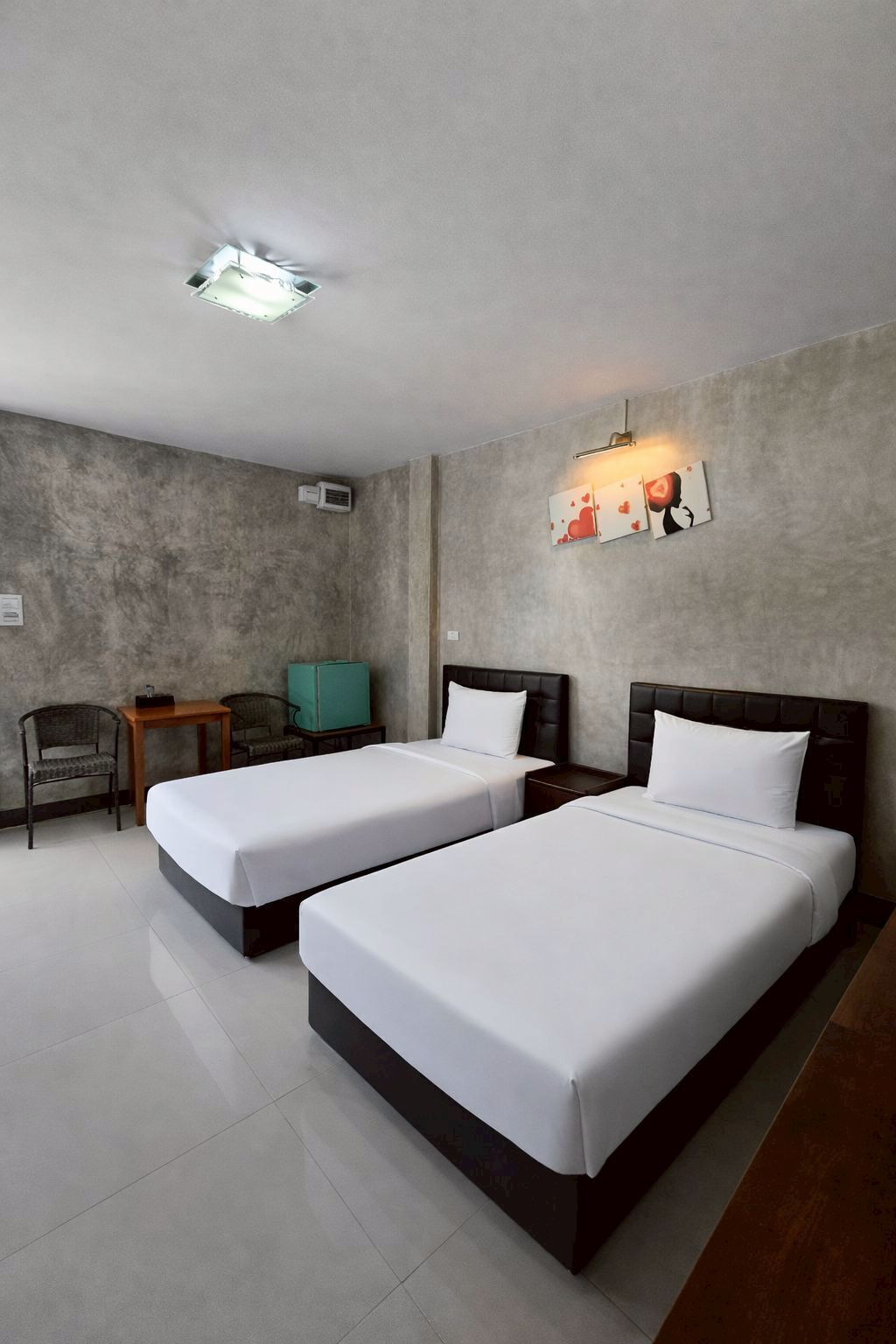 Een hotelkamer met twee bedden, een kleine tafel, twee stoelen, een wandlamp en een plafondlamp.