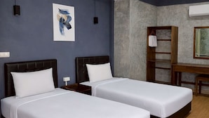 Una camera d'albergo con due letti, una scrivania, una sedia, un armadio e un quadro appeso al muro.