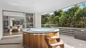 Ein moderner Whirlpool im Freien mit Holzelementen, ein Essbereich mit Tisch und Stühlen und Blick auf üppiges Grün.