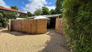 Un espace extérieur clos, avec un sol en gravier, un bâtiment doté d’un toit rouge et une clôture en bambou.