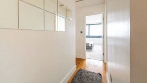 A hallway with a tiled wall, a wooden floor, and a door leading to a room with a bed and a window. - Incredible 3BR Battersea Flat & Spectacular View (Greater London)