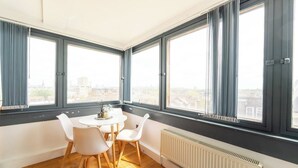 A room with a dining table and chairs, large windows with curtains, and a radiator. - Incredible 3BR Battersea Flat & Spectacular View (Greater London)