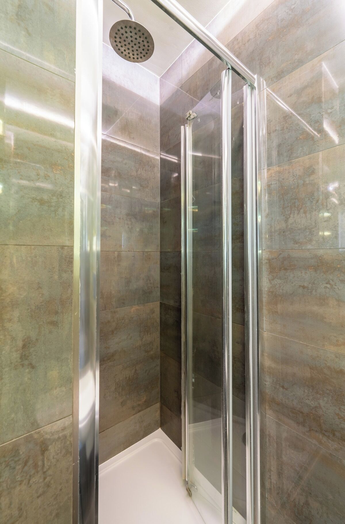 Cabina de ducha con mampara de vidrio, cabezal de ducha de mano y paredes de baldosas de mármol.