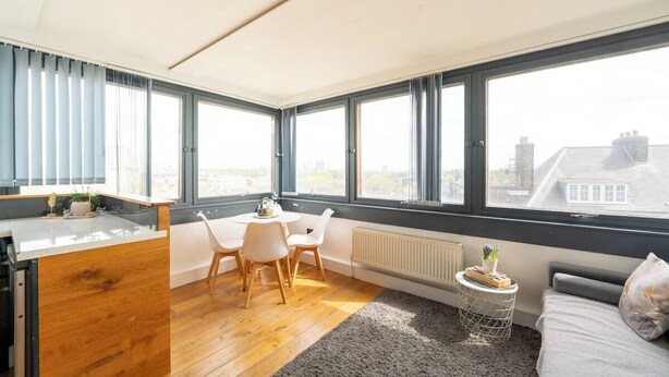 A modern apartment with a kitchen, dining area, and a large window with a city view. - Incredible 3BR Battersea Flat & Spectacular View (Greater London)