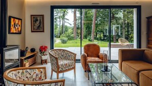A living room with a glass coffee table, two patterned chairs, a brown sofa, a television, and artwork on the wall. - Bread et Couette (Lyon)