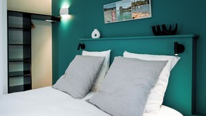 A bed with two pillows, a nightstand, a shelf with decorative items, and a wall-mounted light. - Bread et Couette (Lyon)