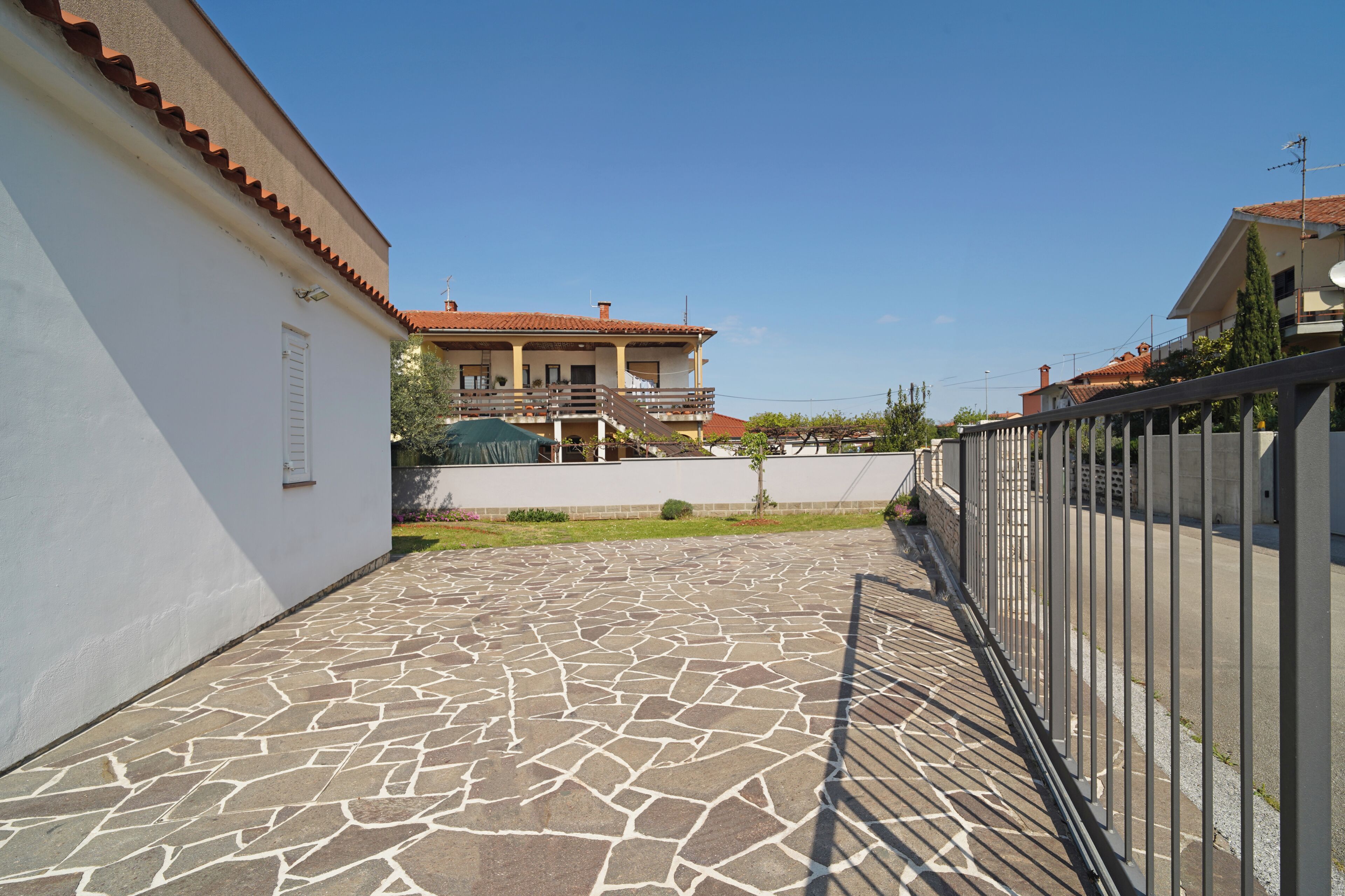 A courtyard with a stone floor, a white wall, and a building with a tiled roof in the background.
