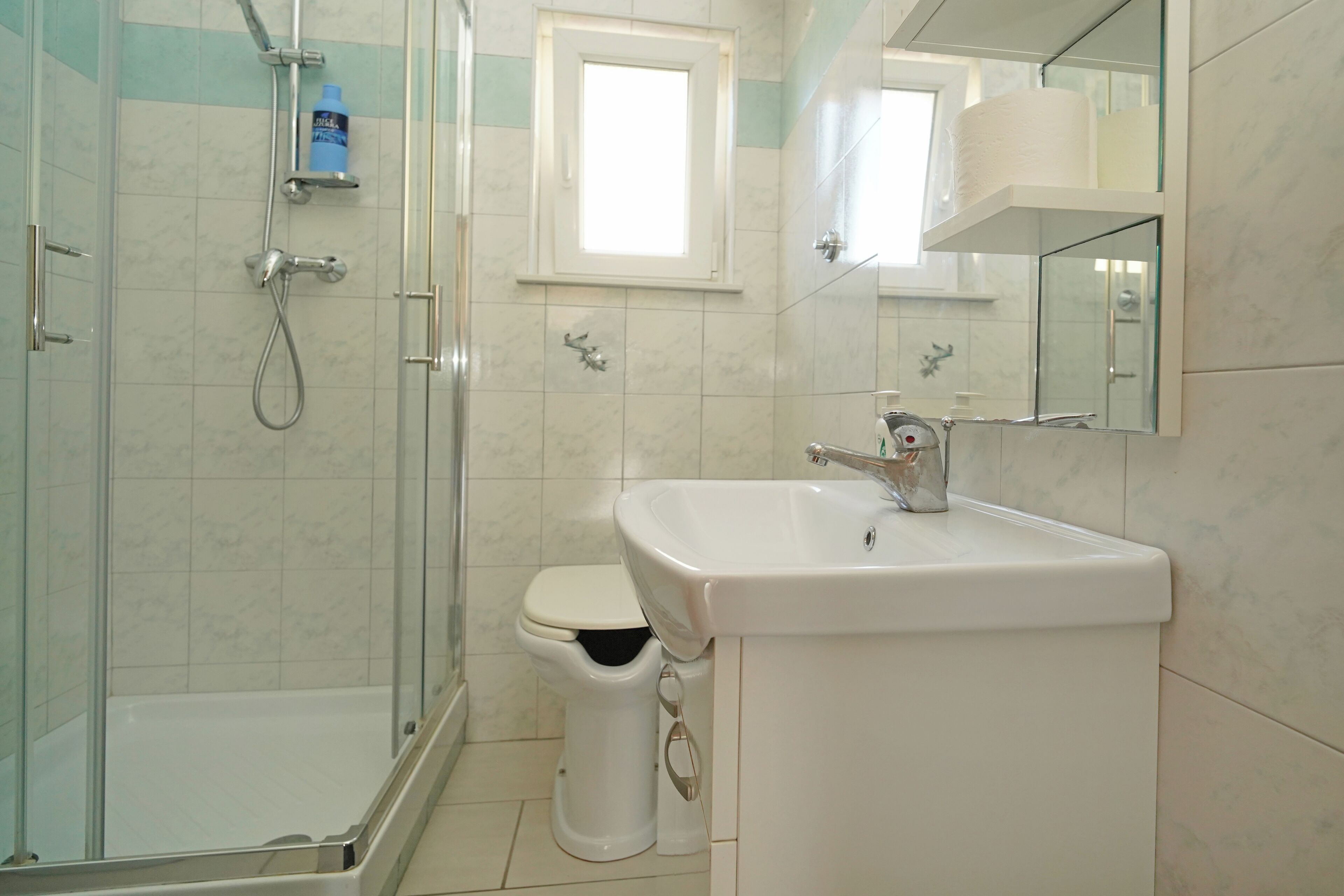 A bathroom with a shower, toilet, sink, and a window.