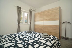 Ein Schlafzimmer mit einem Bett, einem Kleiderschrank, einem Fenster mit Vorhängen und einer Klimaanlage.