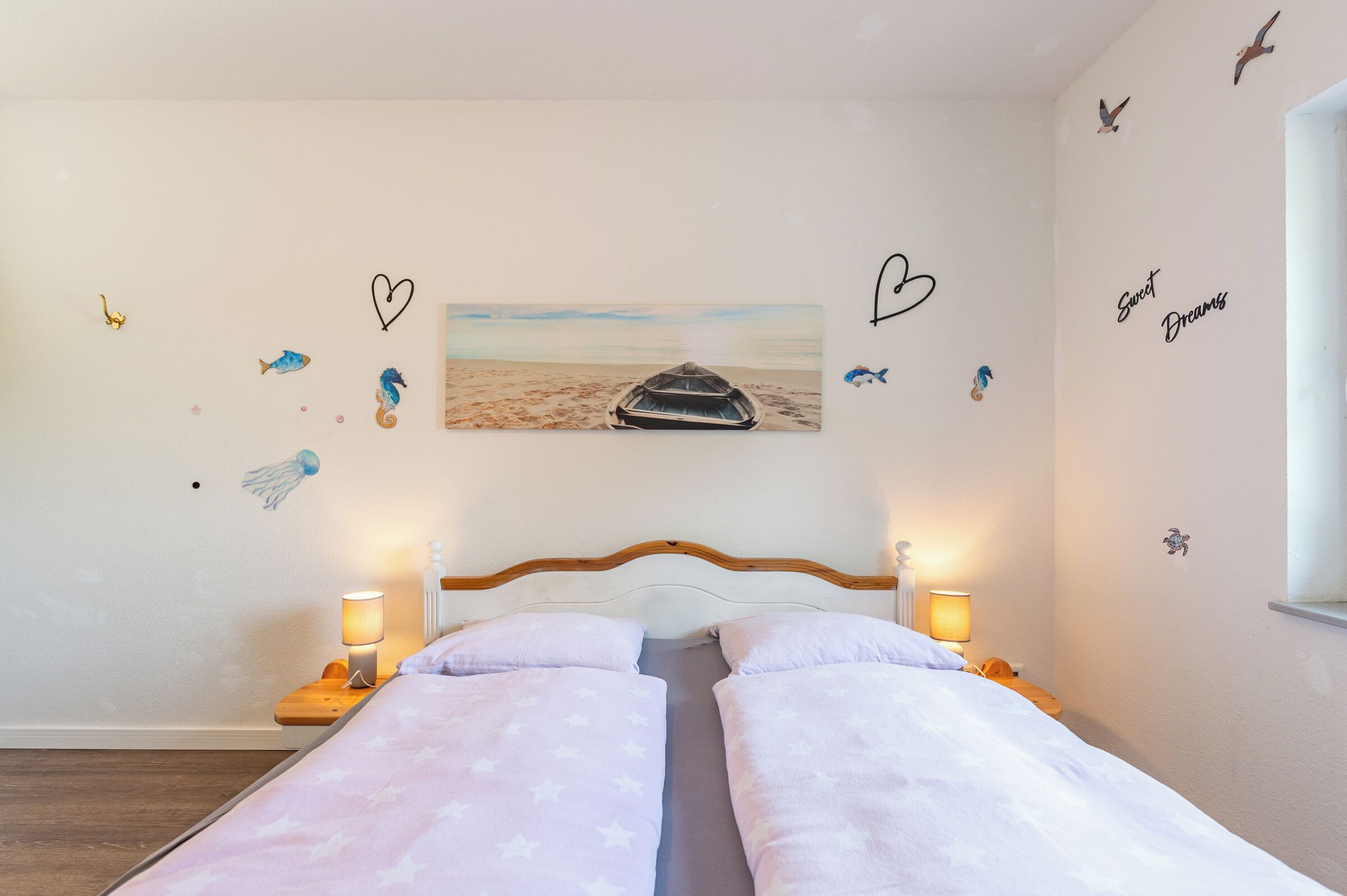 A bedroom with two beds, a painting of a boat on the wall, and decorative wall stickers including hearts and seahorses.