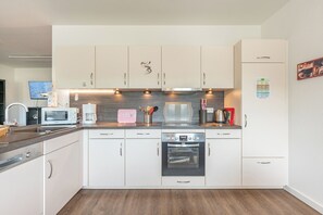 A modern kitchen with white cabinetry, a Bosch microwave, a coffee maker, and a dishwasher. - "Landgang" Vacation Rental in Husum-Schauendahl for up to 5 people (Horstedt-Feld)
