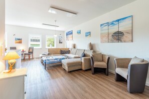 A spacious living area with a sofa set, a coffee table, and a dining table. There are multiple windows providing natural light, and artwork is displayed on the walls. - "Landgang" Vacation Rental in Husum-Schauendahl for up to 5 people (Horstedt-Feld)