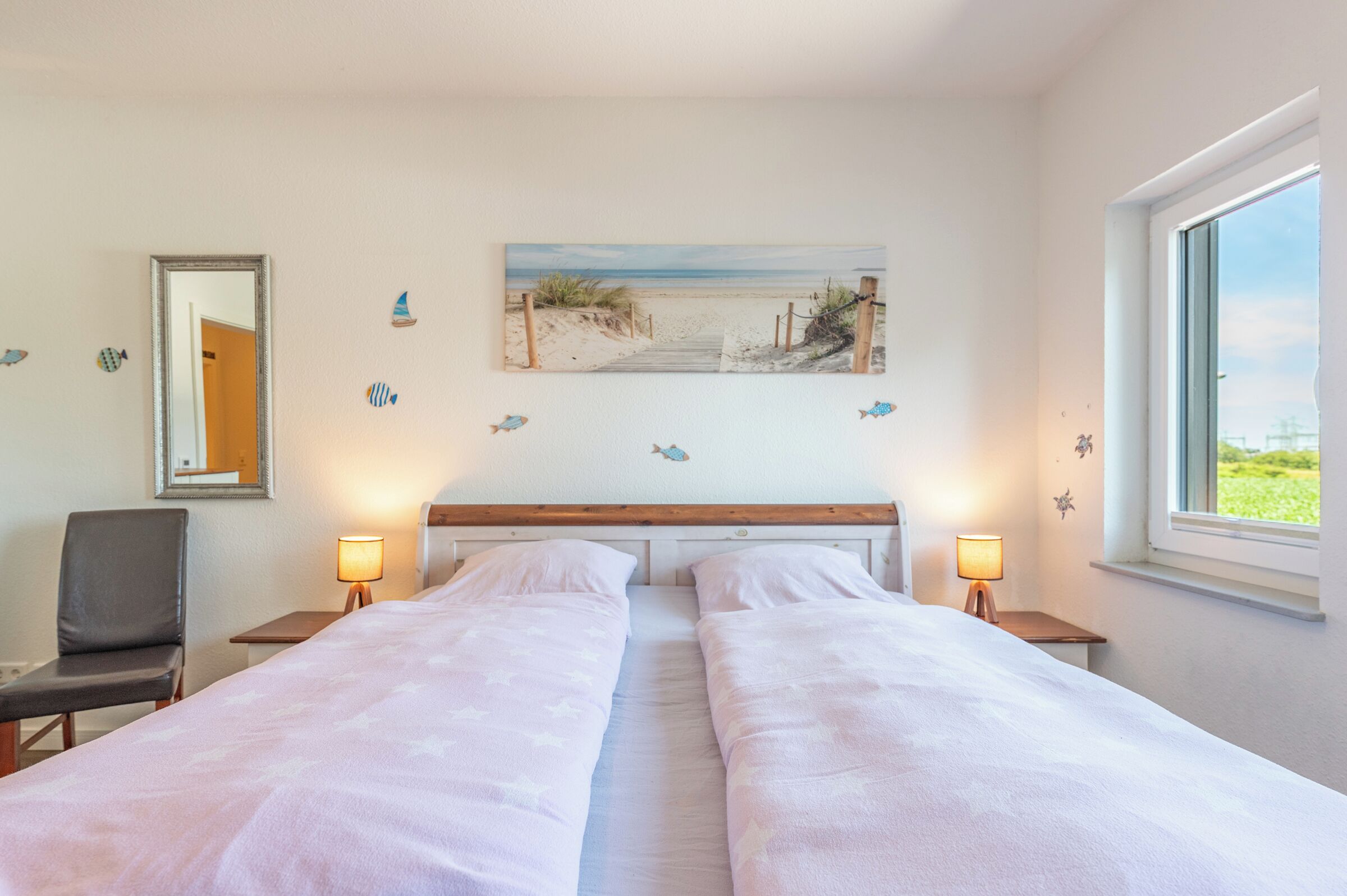 A hotel room with two beds, a wooden headboard, a beach-themed wall art, and a window with a view.