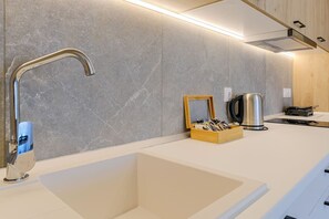 A modern kitchen with a built-in sink, a kettle, and a wooden box with utensils. - DeMar No 2 by RentalsPro - Agios Nikolaos (Agios Nikolaos)