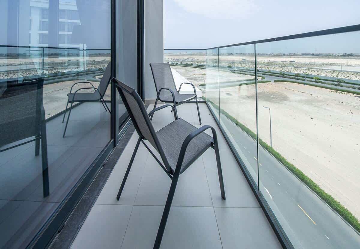 A balcony with two chairs, a glass railing, and a view of a sandy landscape.