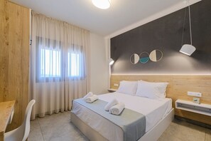 A hotel room with a bed, a desk, a chair, and a window with curtains.